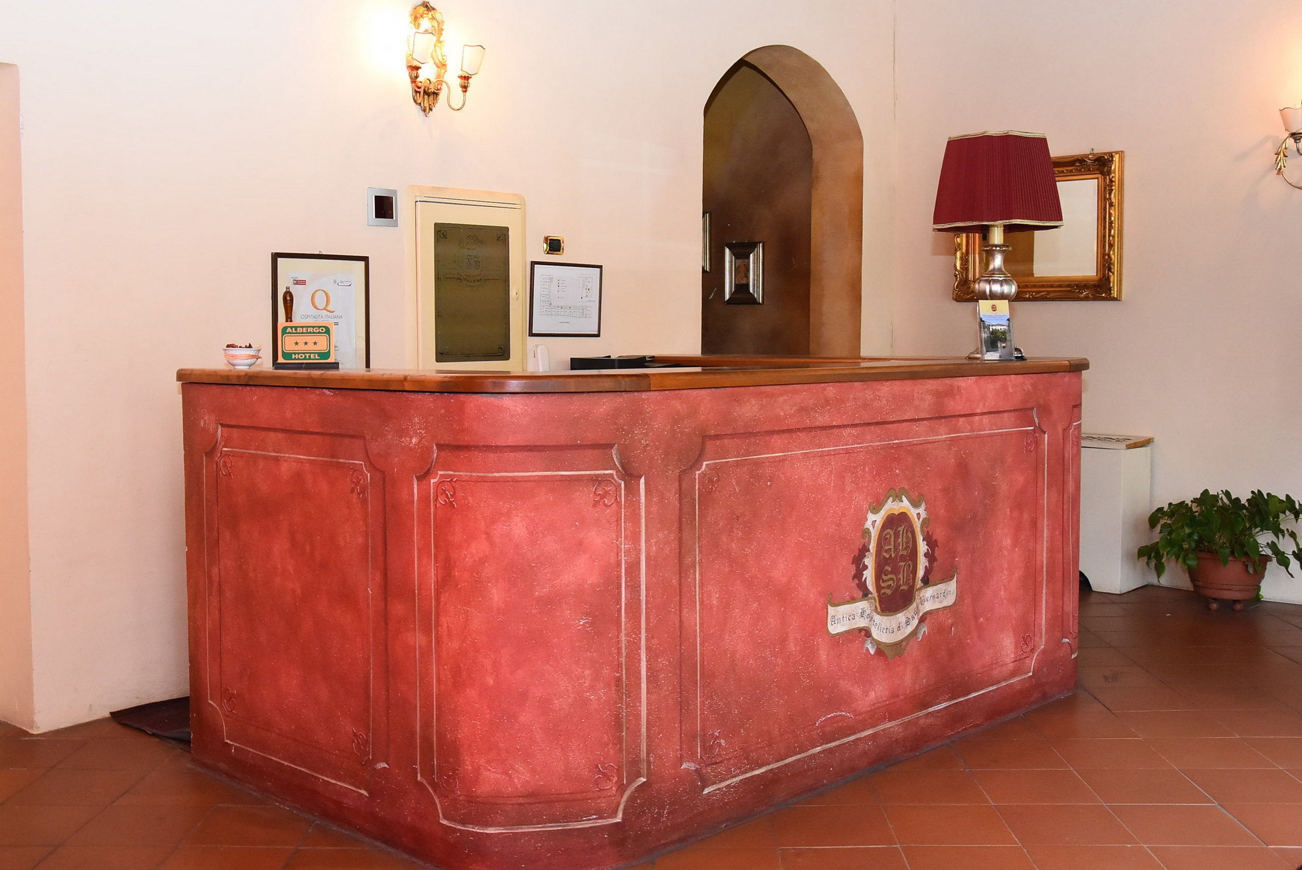 A reception desk with a red finish, a framed certificate, a lamp, and a potted plant.