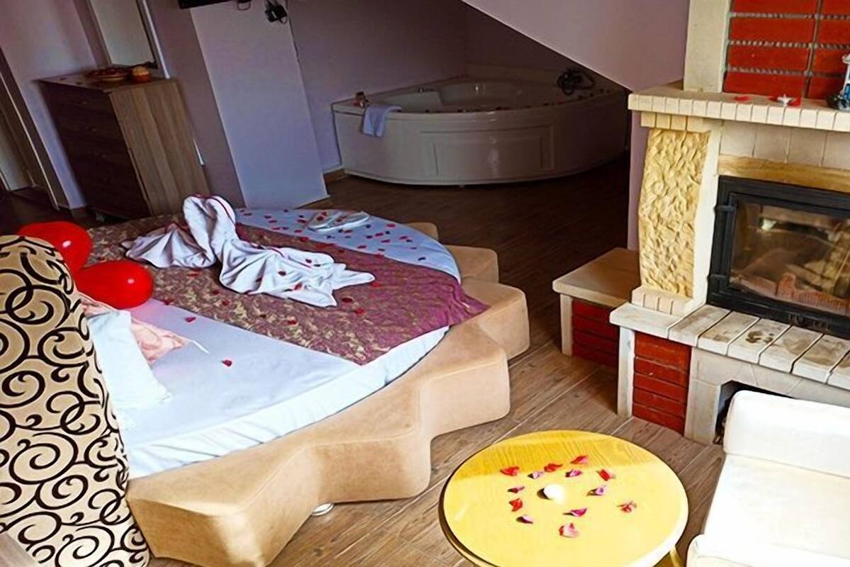 Quarto com cama, mesa redonda pequena, sofá, lareira e banheira.