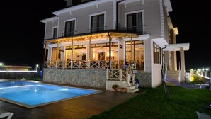 A two-story house with a swimming pool, a covered patio, and a well-lit interior.