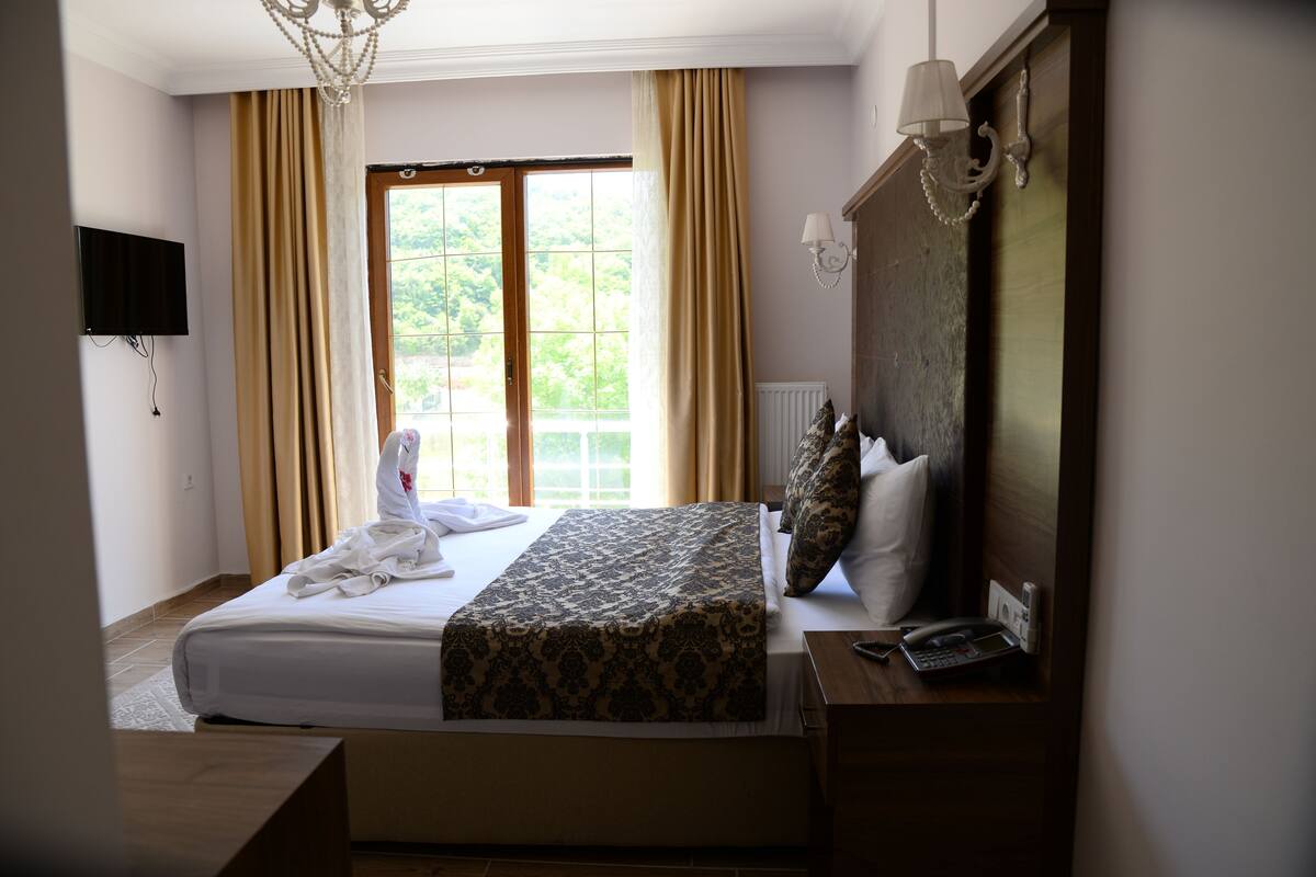 Quarto de hotel com cama, mesa de cabeceira com abajur, televisão na parede e janela com cortinas.