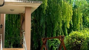 A residential property with a covered porch, a swing set, and a lush green tree.