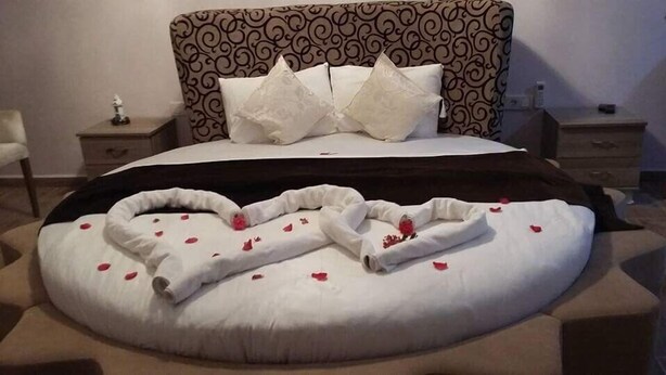 A bed with a heart-shaped arrangement of towels and rose petals.