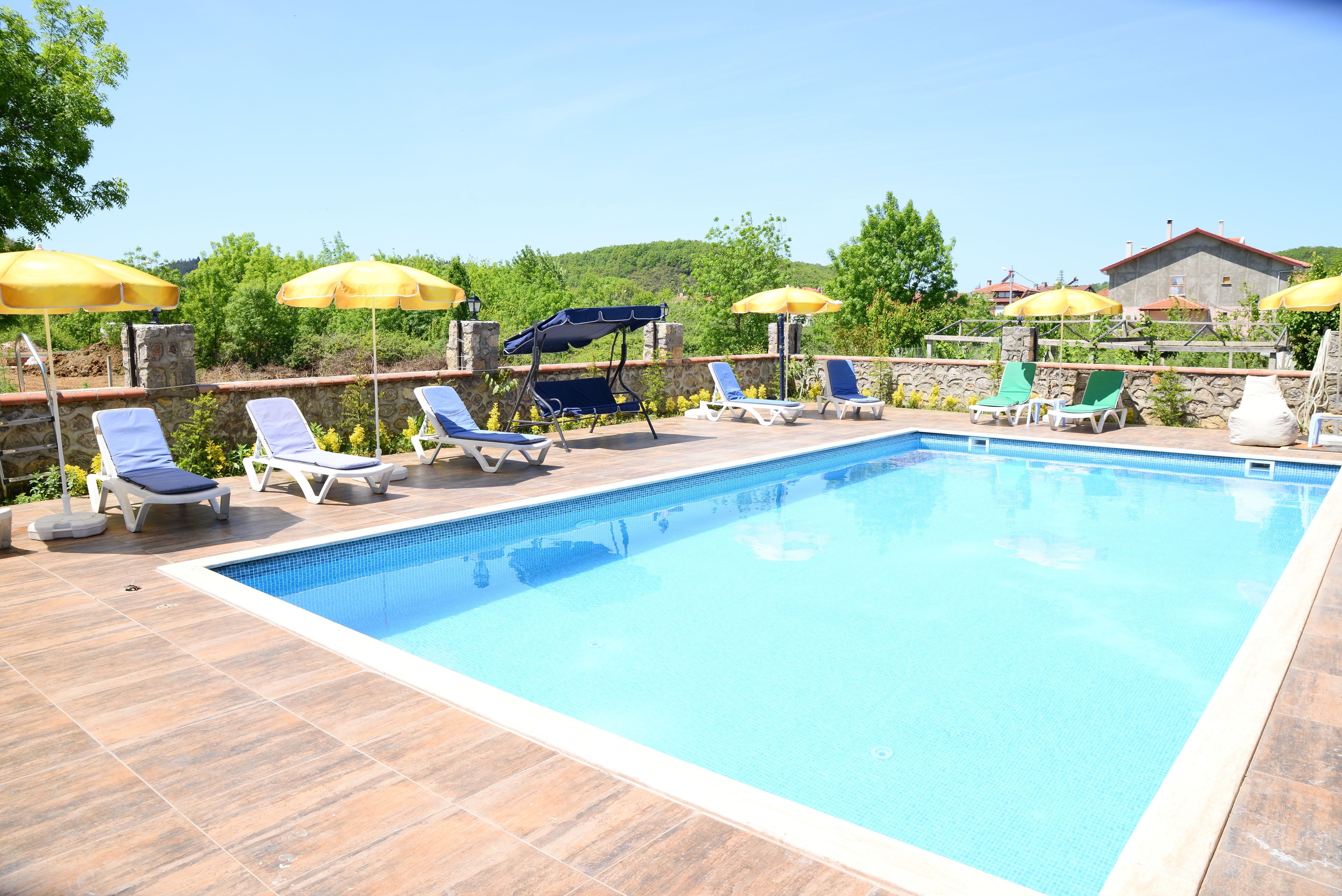 A swimming pool with lounge chairs and umbrellas, surrounded by stone walls and greenery.