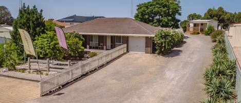 A single-story building with a garage, surrounded by a gravel driveway and a wooden fence.