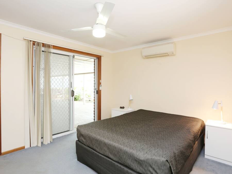 Un dormitorio con cama, mesita de noche, ventilador de techo y puerta corrediza de vidrio que da a un área exterior.