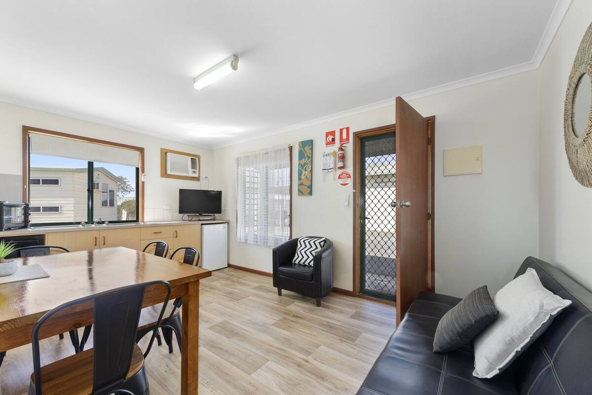A compact living space with a dining area, a sofa, a television, and a kitchen area.