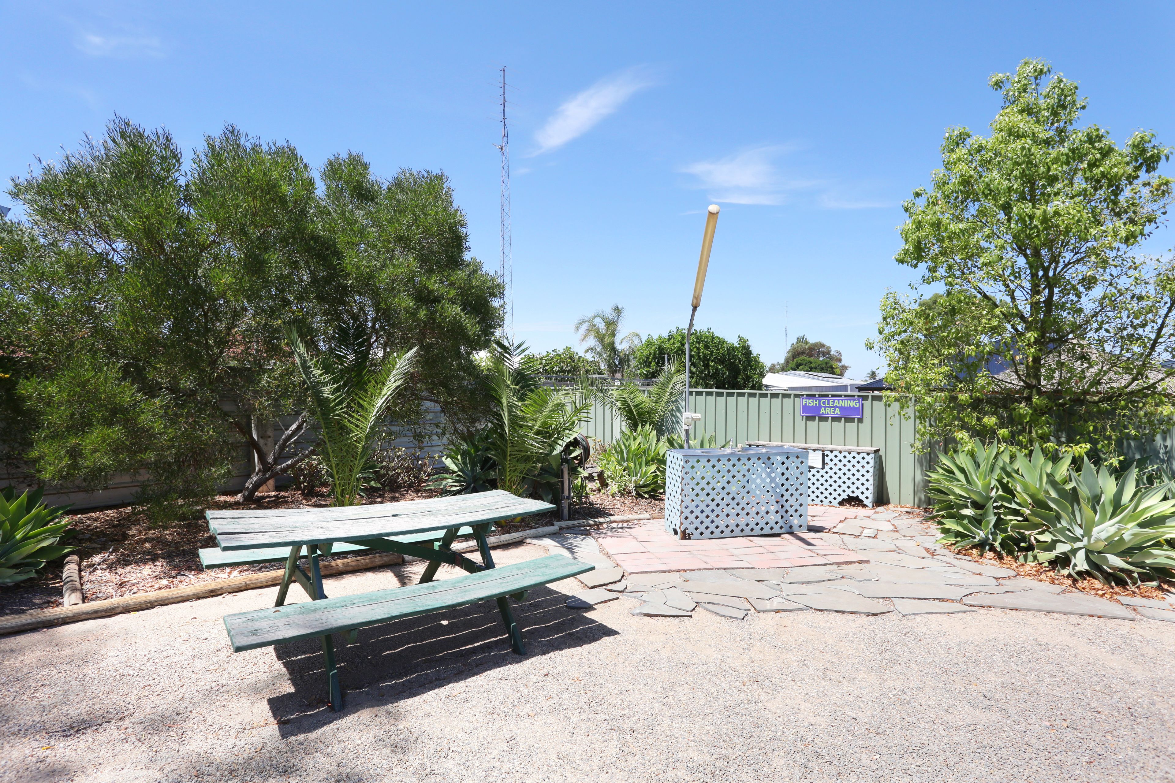 A picnic area with green benches, a stone pathway, and a fenced fish cleaning area.