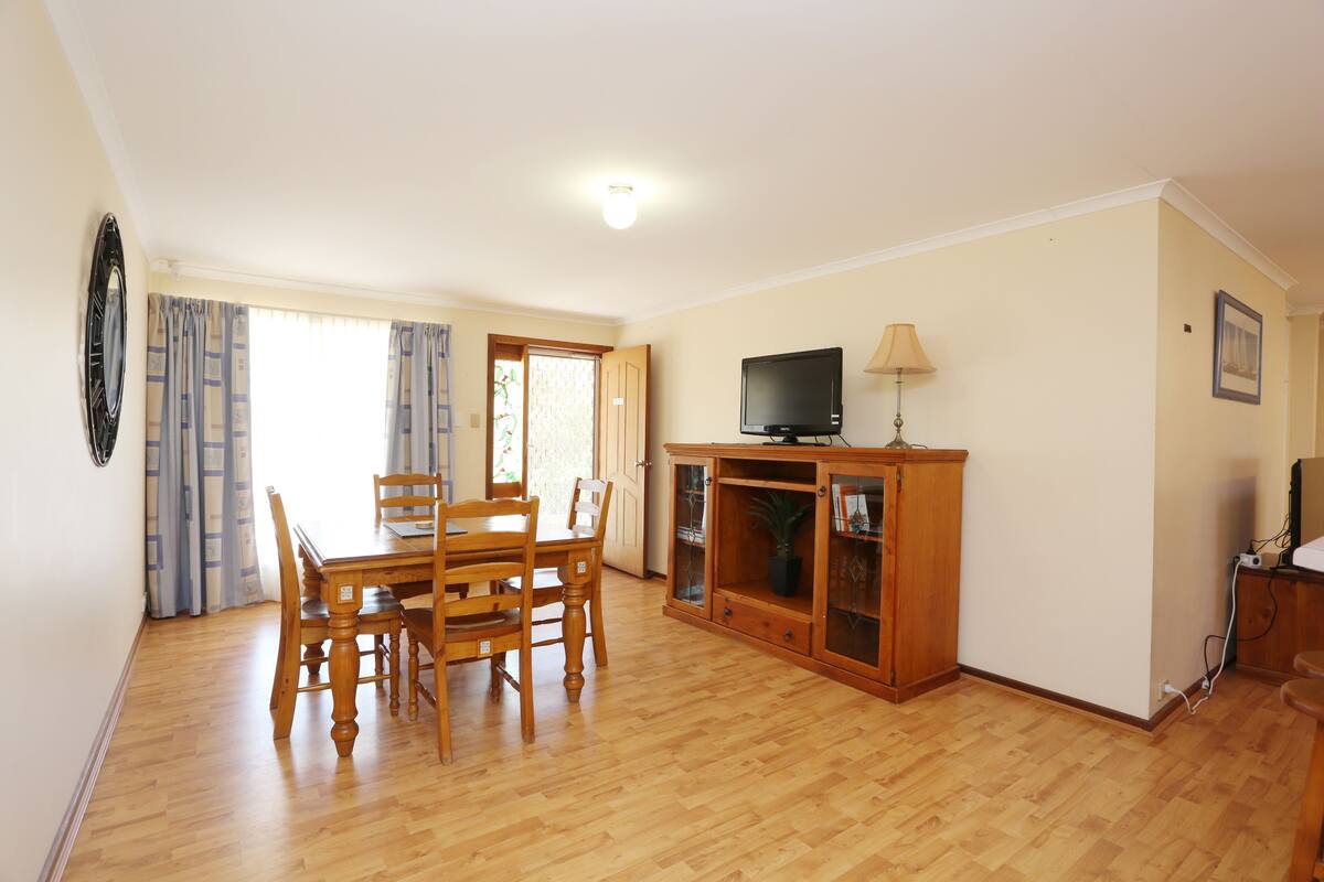 A dining area with a wooden table and chairs, a television on a cabinet, and a door leading to another room.