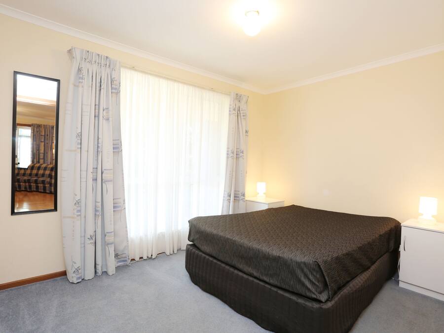 A bedroom with a bed, a nightstand, a lamp, a mirror, and a window with curtains.