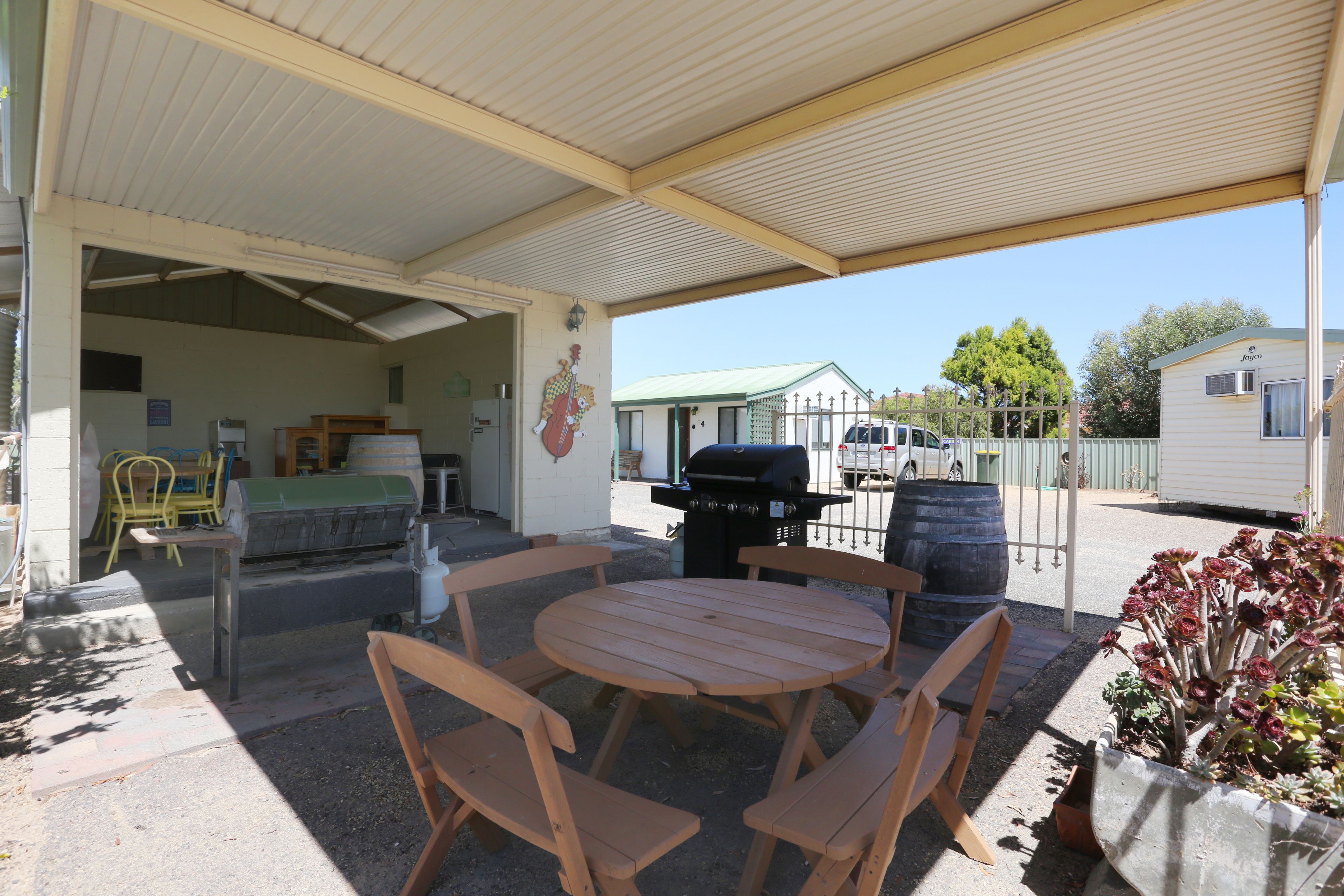 Un patio exterior techado con una mesa y sillas de madera, una parrilla y una planta en maceta.