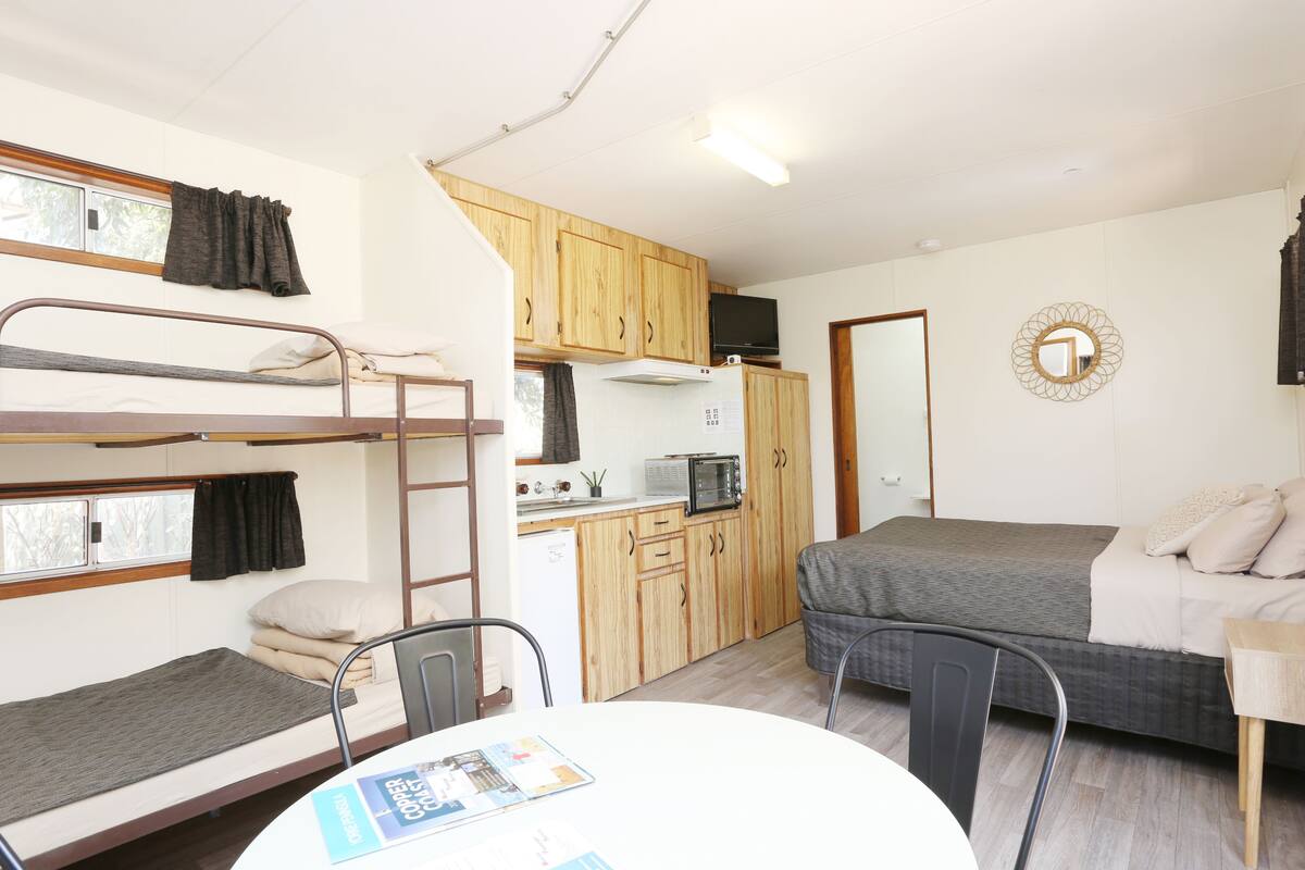 A compact room with bunk beds, a kitchenette, a dining table, and a single bed.