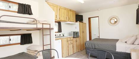 A compact room with bunk beds, a kitchenette, a dining table, and a single bed.