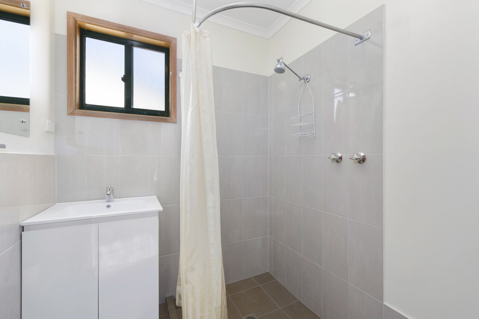 Een badkamer met een douche, een wastafel en een raam.