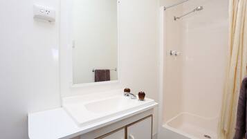 A bathroom with a white sink, a mirror, a shower with a glass door, and a towel hanging on the wall.
