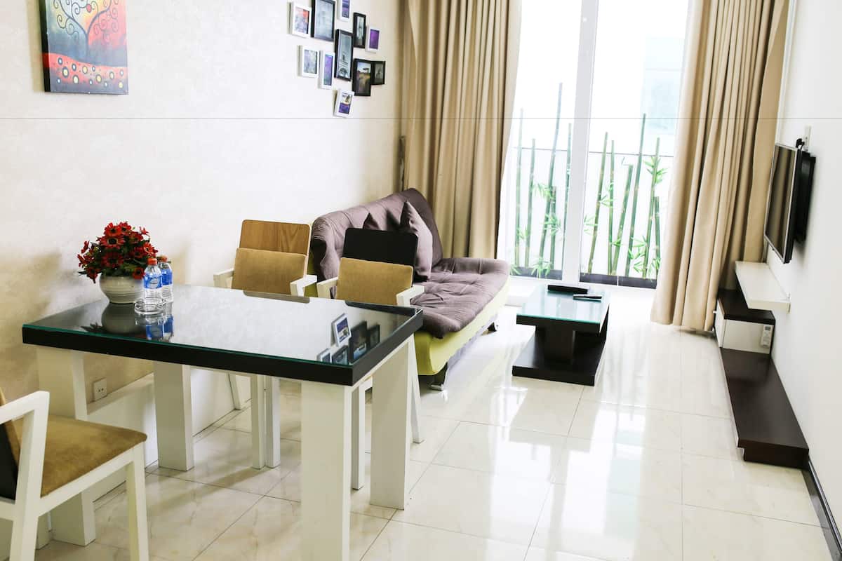 A modern living room with a glass dining table, a sofa, and a TV mounted on the wall.