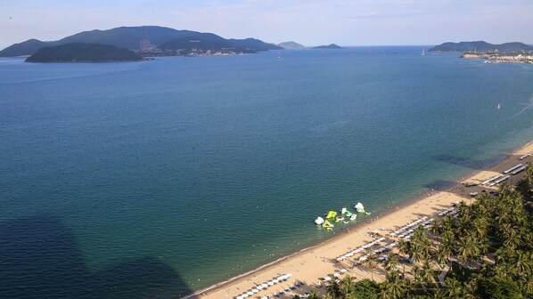 A beach with umbrellas and people, a clear sky, and distant mountains. - Gold Ocean Nha Trang (Nha Trang)