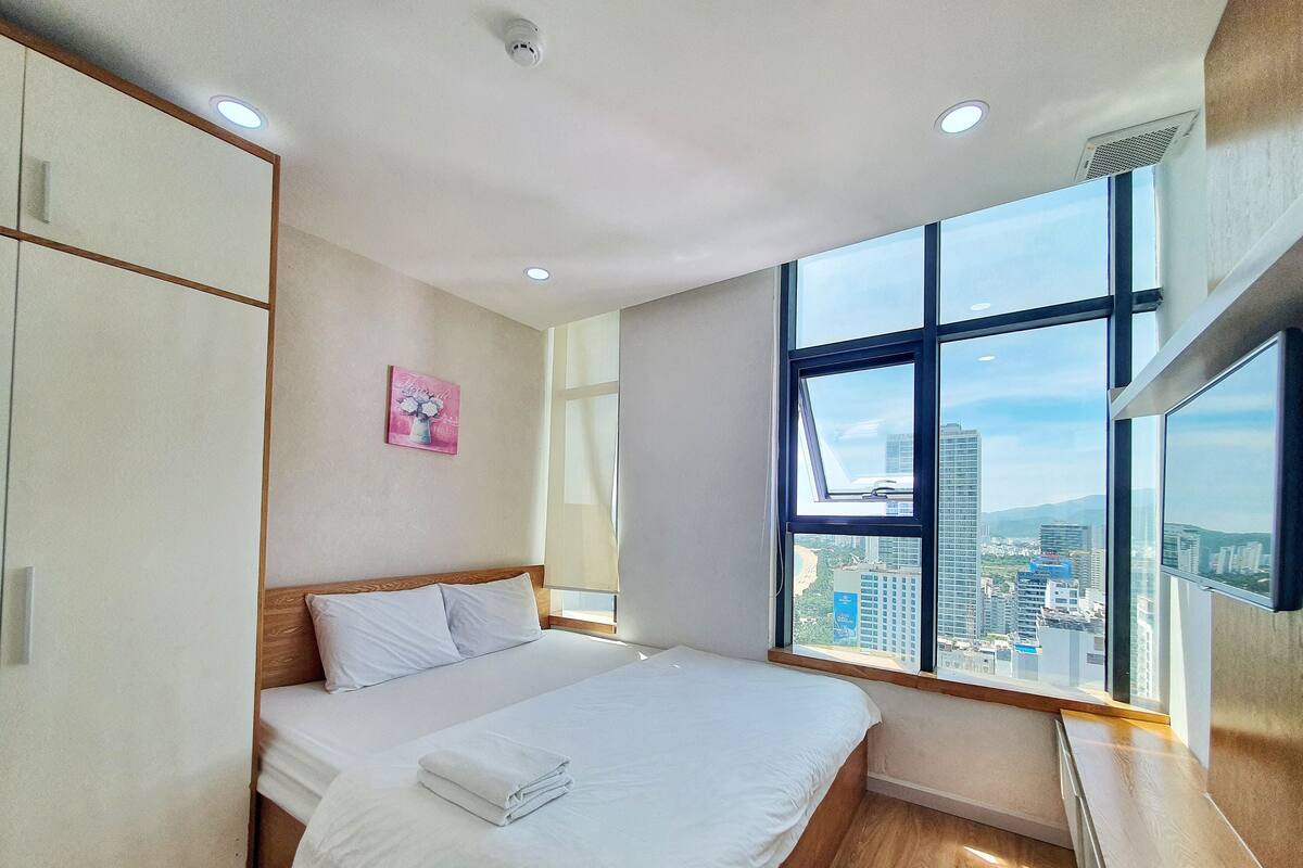 A modern hotel room with a large bed, a wardrobe, and a window with a city view.