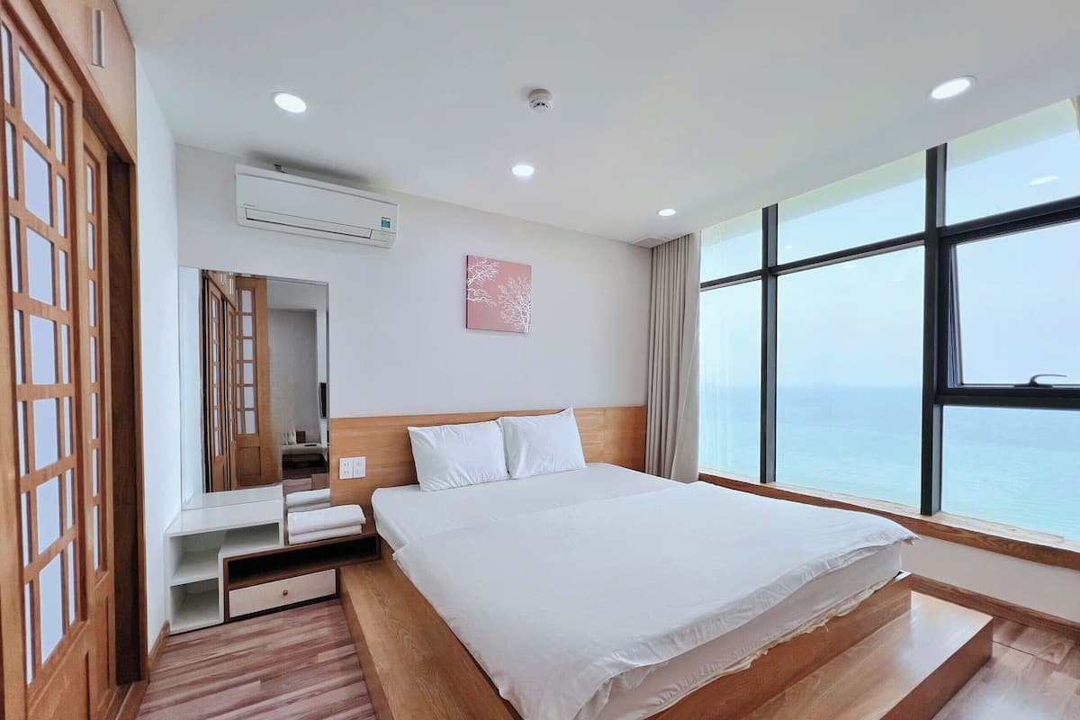 A hotel room with a large bed, a wooden floor, a view of the sea, and a modern design.
