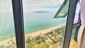 Blick aus einem Fenster auf einen Strand mit Palmen und einem klaren Himmel.