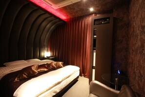 A hotel room with a curved ceiling, a bed with white linens, a brown leather headboard, and a glass table with a chair. - HOTEL EDOYADO - Adults Only (Tokyo)