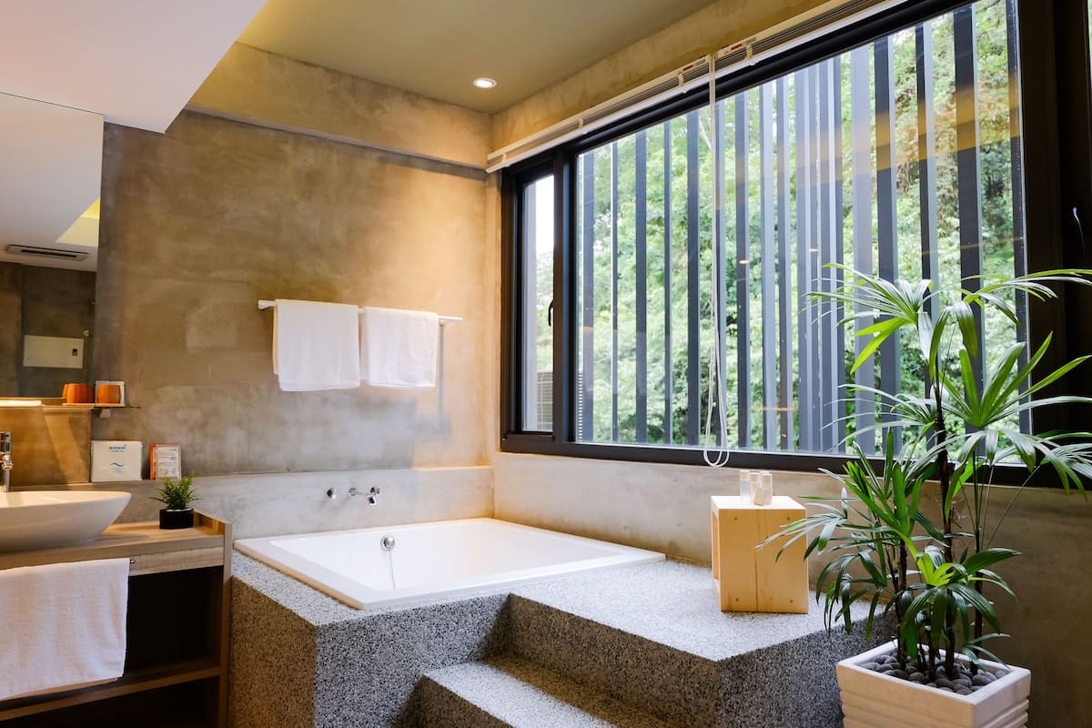 A modern bathroom with a large bathtub, a sink, and a window with vertical blinds.