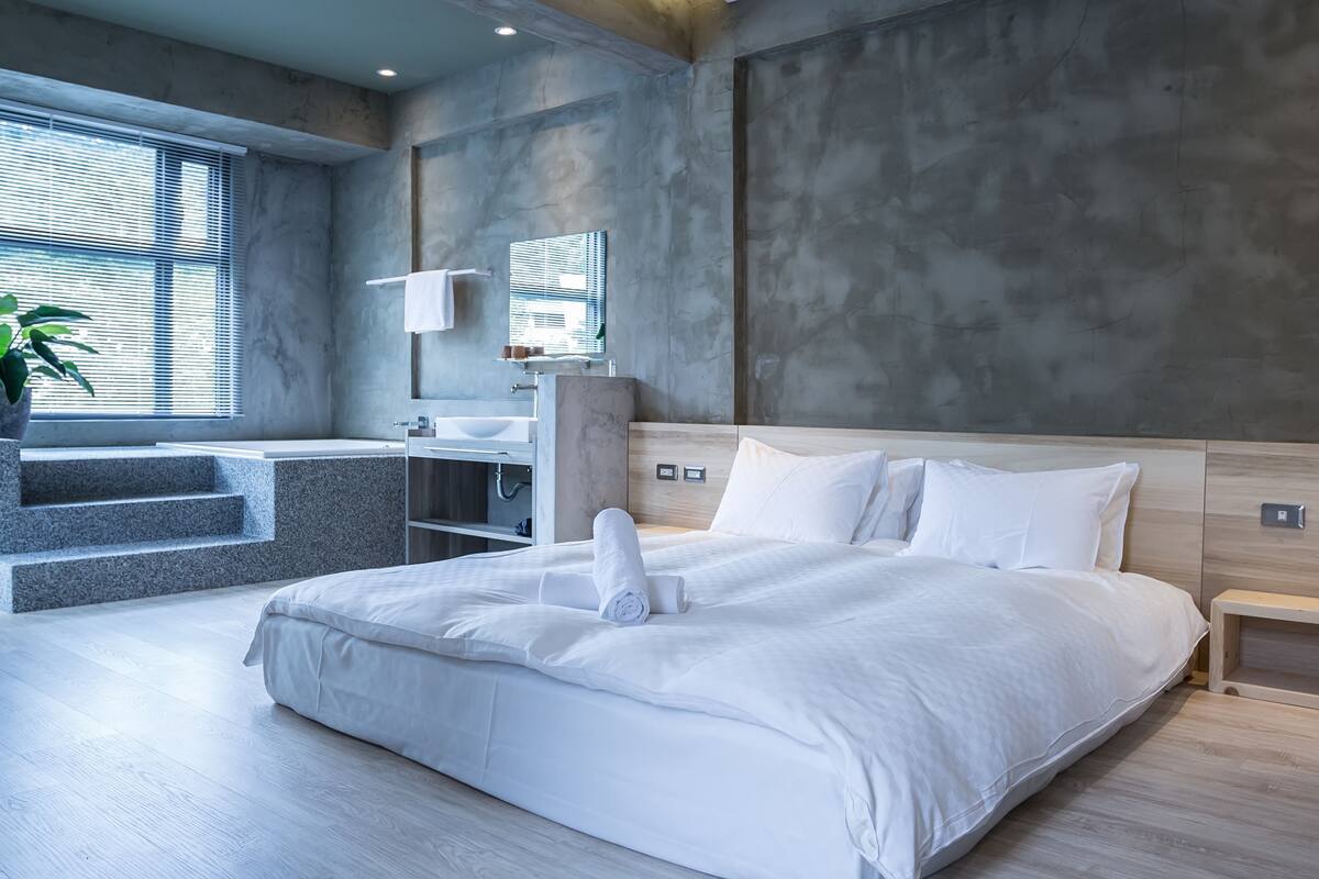 A modern hotel room with a large bed, a bathroom with a sink and mirror, and a staircase leading to an outdoor area.