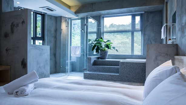 A modern hotel room with a large bed, a potted plant, and a view of the outdoors through a large window. - Shao Guang 188 (Yuchi)