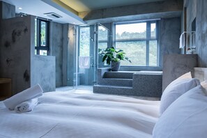 Una habitación de hotel moderna con una cama grande, una planta en maceta y vistas al exterior a través de un ventanal.