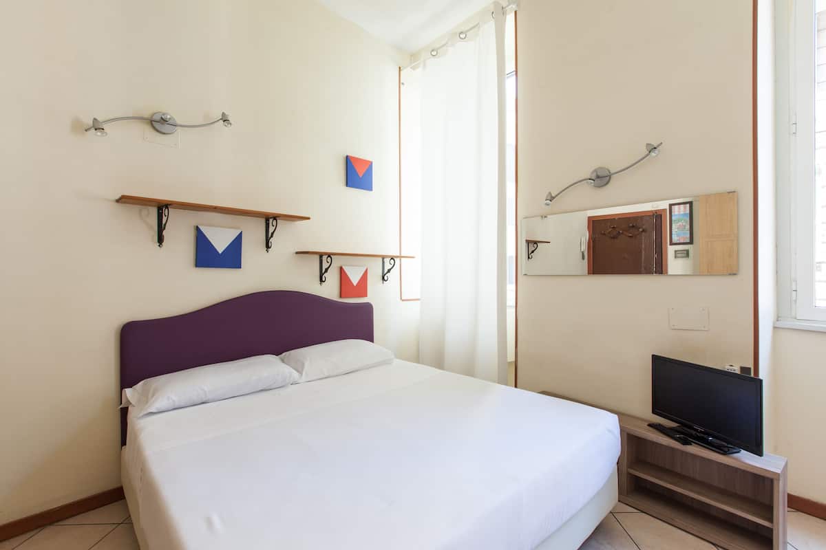 A hotel room with a bed, a television on a wooden stand, and artwork on the walls.