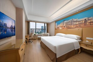 A hotel room with a large bed, a desk, a chair, a TV, and a window with a city view. - Vienna International Qianhai Branch (Shenzhen)