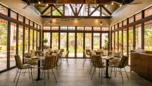 A spacious indoor dining area with large windows, wicker chairs, and tables set for dining. - Aureo La Union (San Fernando)