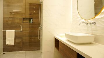 A modern bathroom with a glass-enclosed shower, a marble-tiled wall, a white sink, and a wooden vanity.