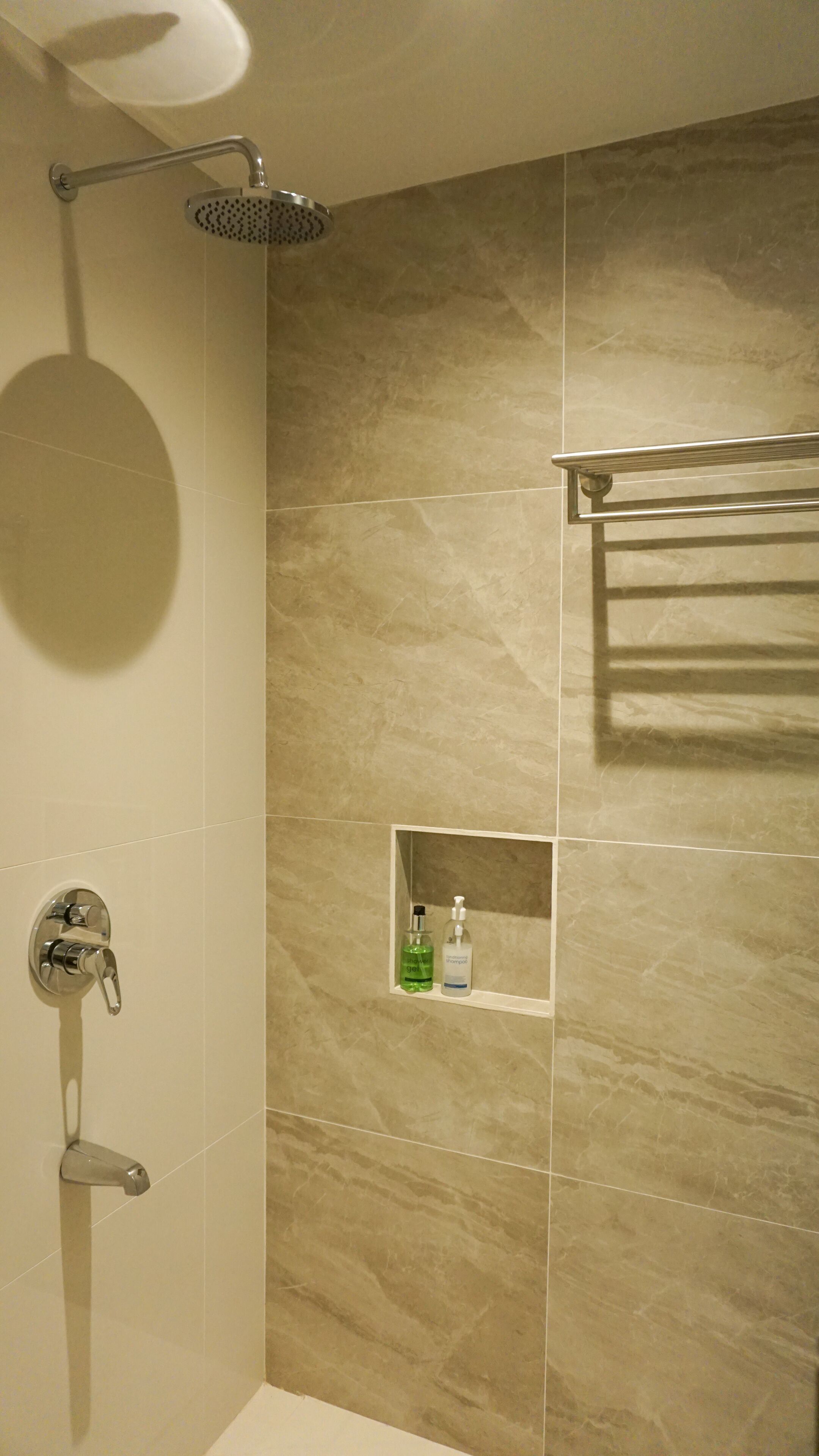 A bathroom with a shower, a towel rack, and a shelf with toiletries.