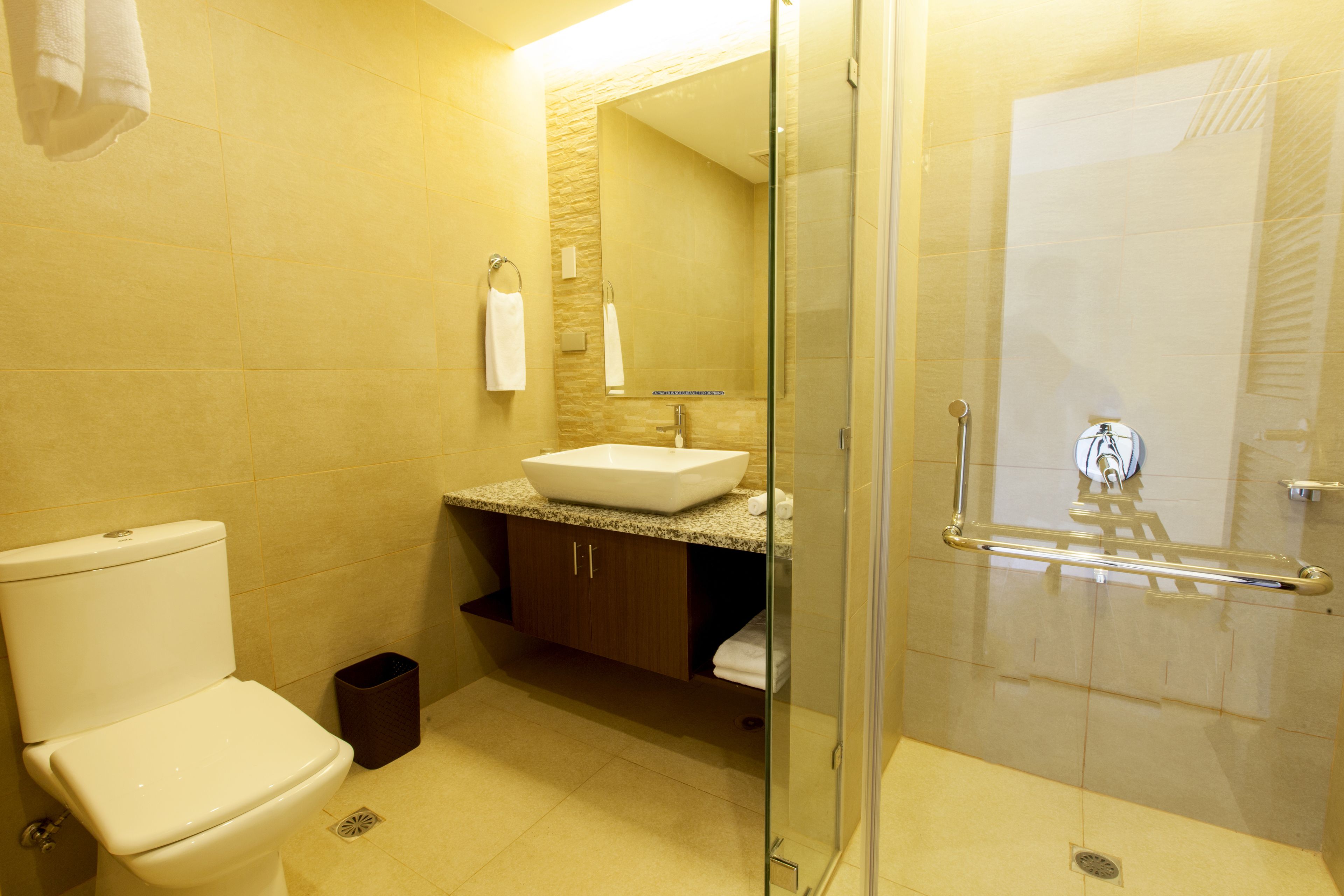 A bathroom with a toilet, sink, mirror, and glass-enclosed shower.