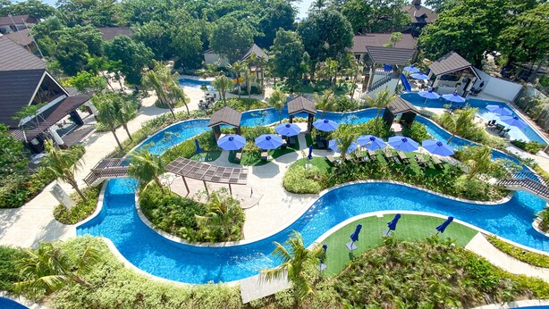 A resort with multiple swimming pools, lush greenery, and shaded areas with umbrellas. - Aureo La Union (San Fernando)