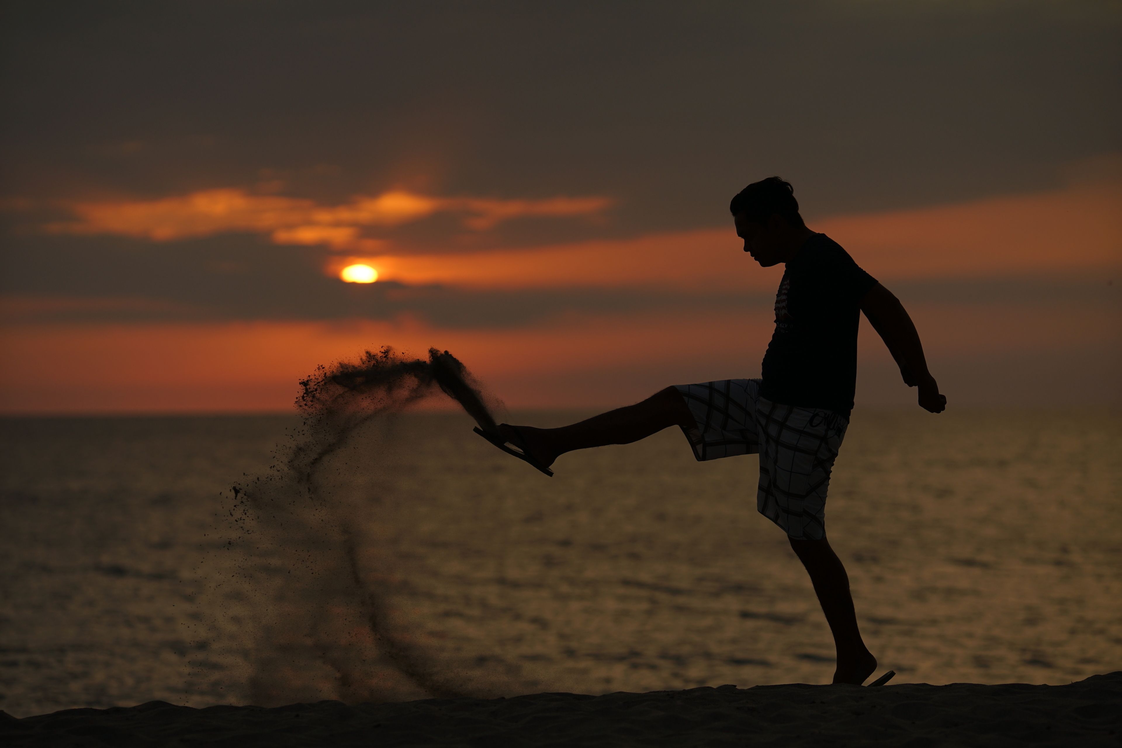 Une personne effectuant un mouvement de pied (donnant un coup de pied) sur une plage au coucher du soleil.