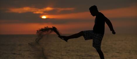Une personne effectuant un mouvement de pied (donnant un coup de pied) sur une plage au coucher du soleil.