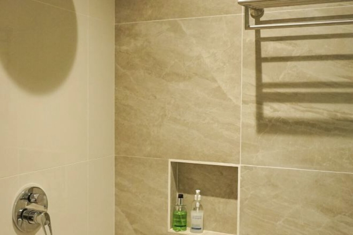 A bathroom with beige tiles, a shower area, and a shelf with two bottles of liquid.