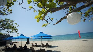A beach with lounge chairs and blue umbrellas, a clear sky, and a calm sea. - Aureo La Union (San Fernando)