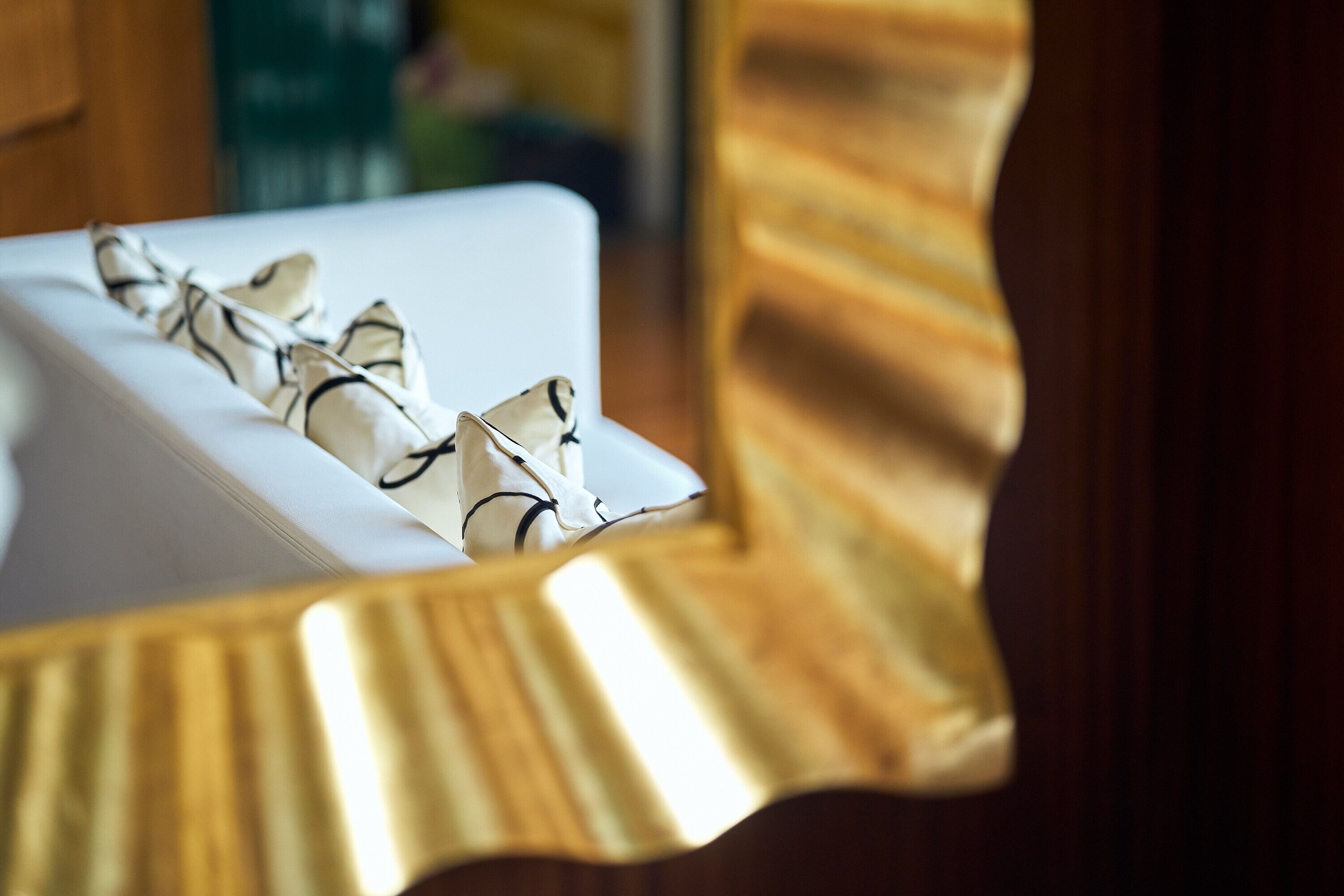 A white bed with a patterned pillow and a gold-framed mirror reflecting part of the room.