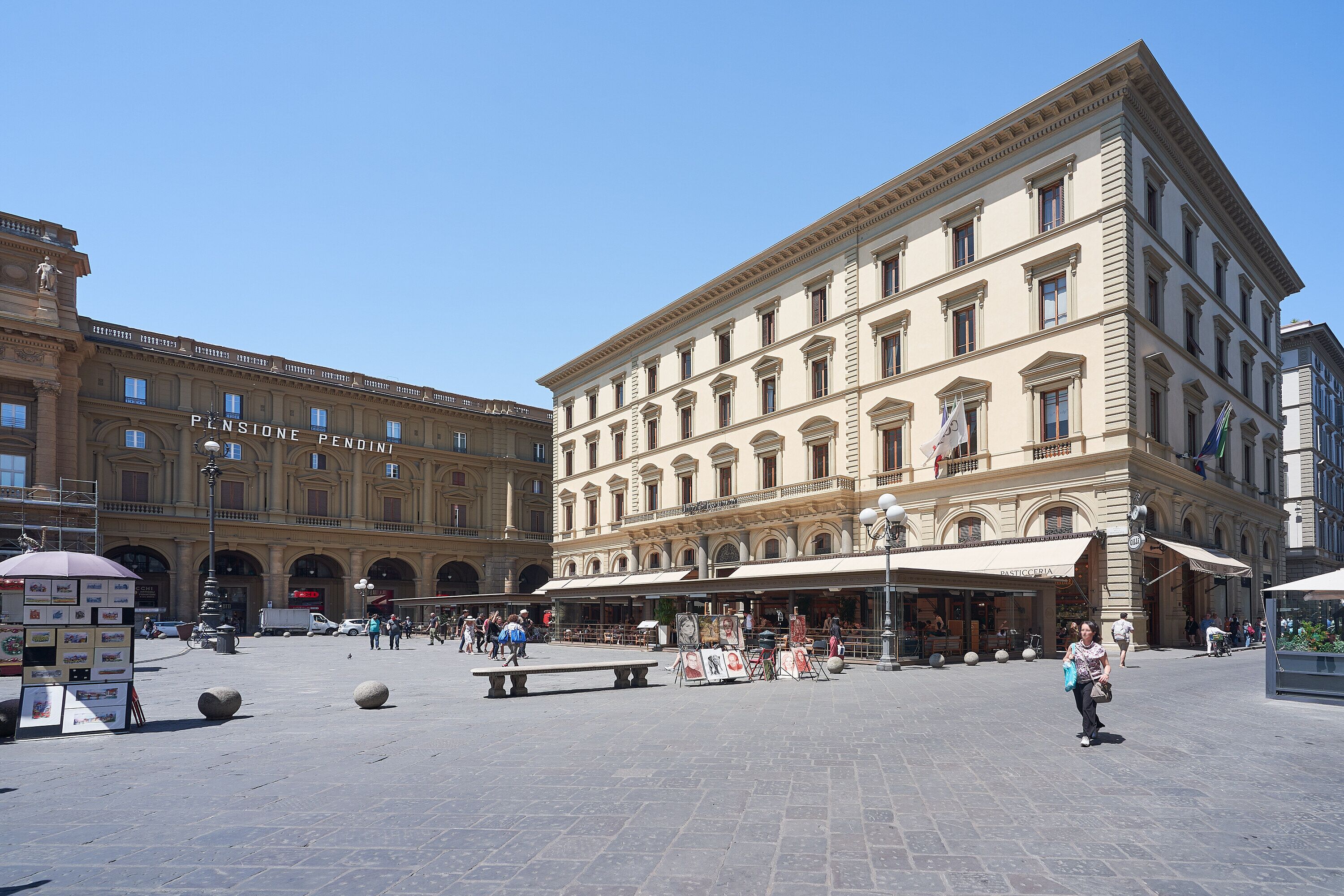 A spacious public square with historic buildings, outdoor seating, and a fountain.