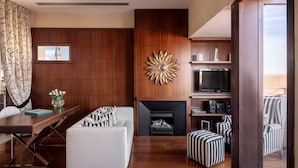 A modern living room with a fireplace, a TV, and striped ottomans. - Repubblica Firenze Luxury Apartments | UNA ESPERIENZE (Florence)