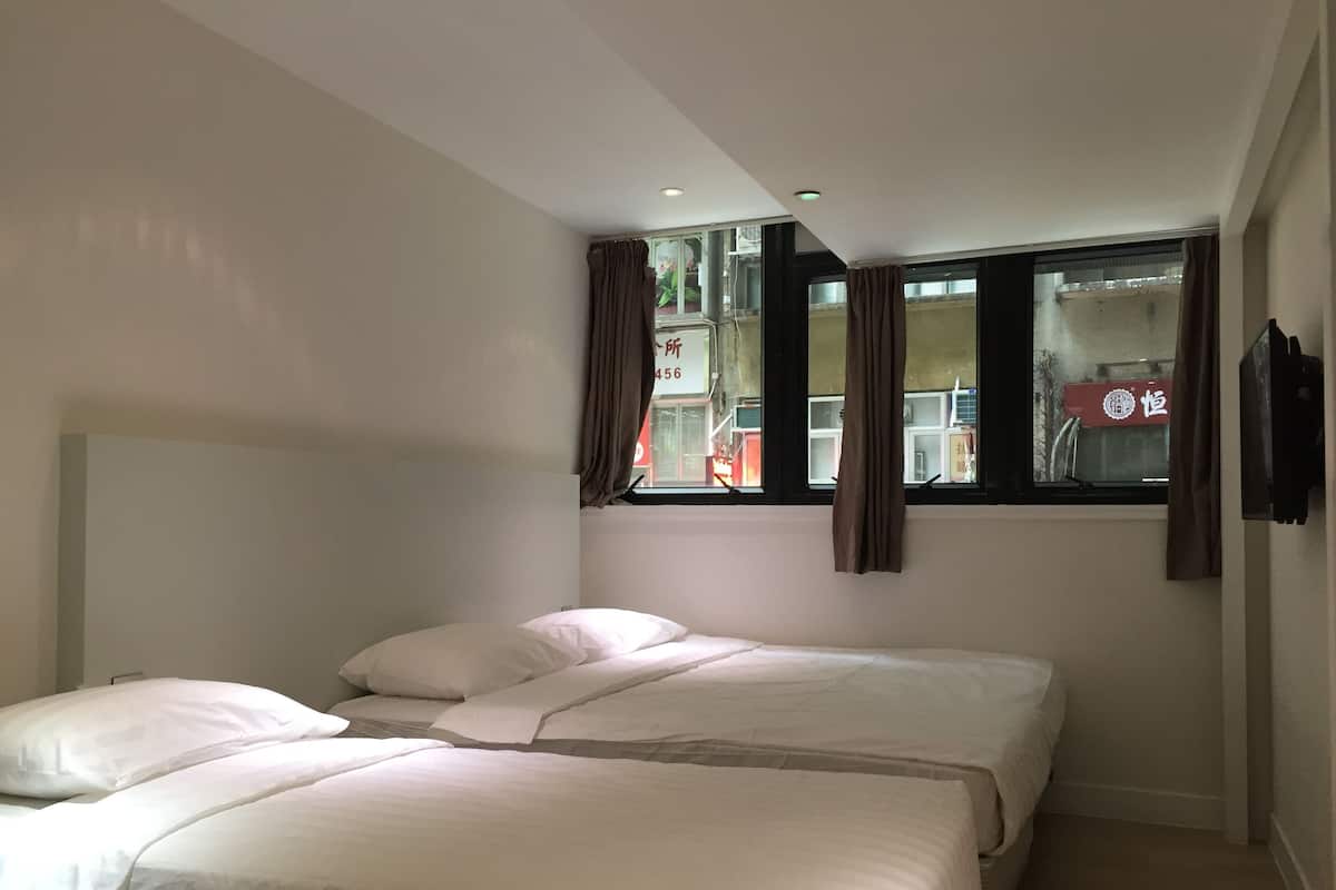 A hotel room with two beds, a window with curtains, and a wall-mounted TV.