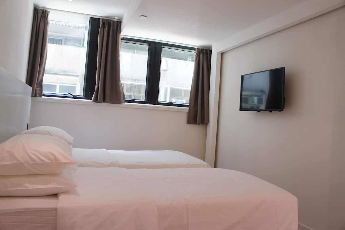 A hotel room with two beds, a television on the wall, and a window with curtains.
