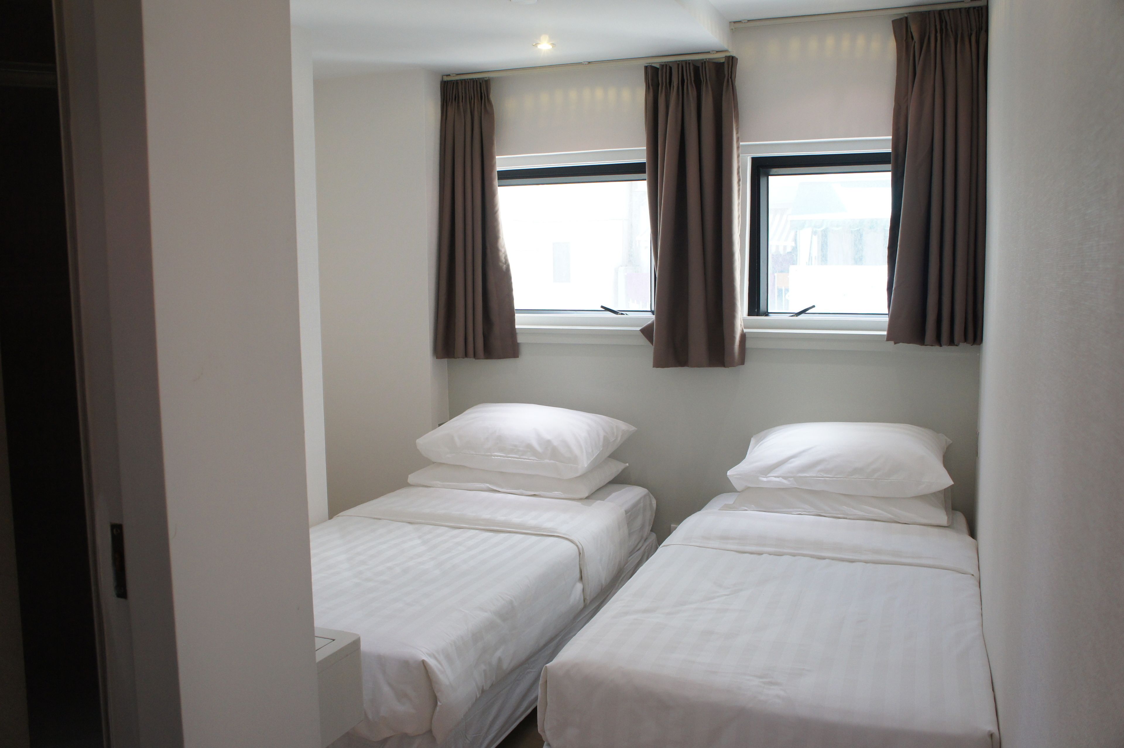 A small, clean room with two single beds, a window with curtains, and a door.