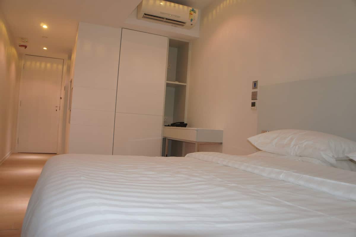 A hotel room with a bed, a wardrobe, a desk, and a wall-mounted air conditioner.