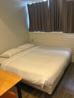A single bed with white bedding, a wooden nightstand, and a window with curtains.
