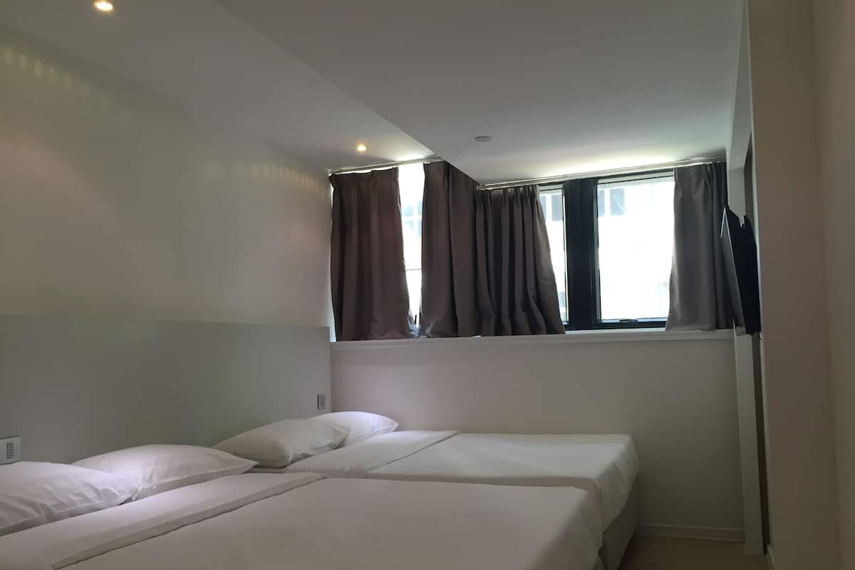 A hotel room with two beds, a window with curtains, and a ceiling light.