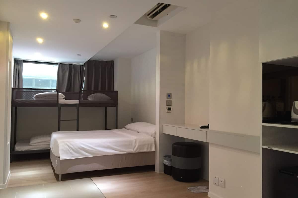 A compact hotel room with bunk beds, a small desk, and a window with curtains.