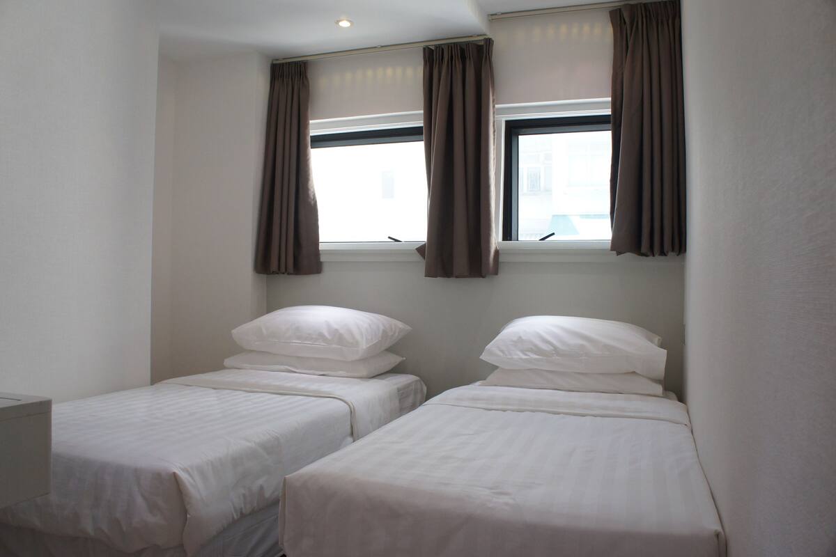 A room with two single beds, a window with curtains, and a white wall.